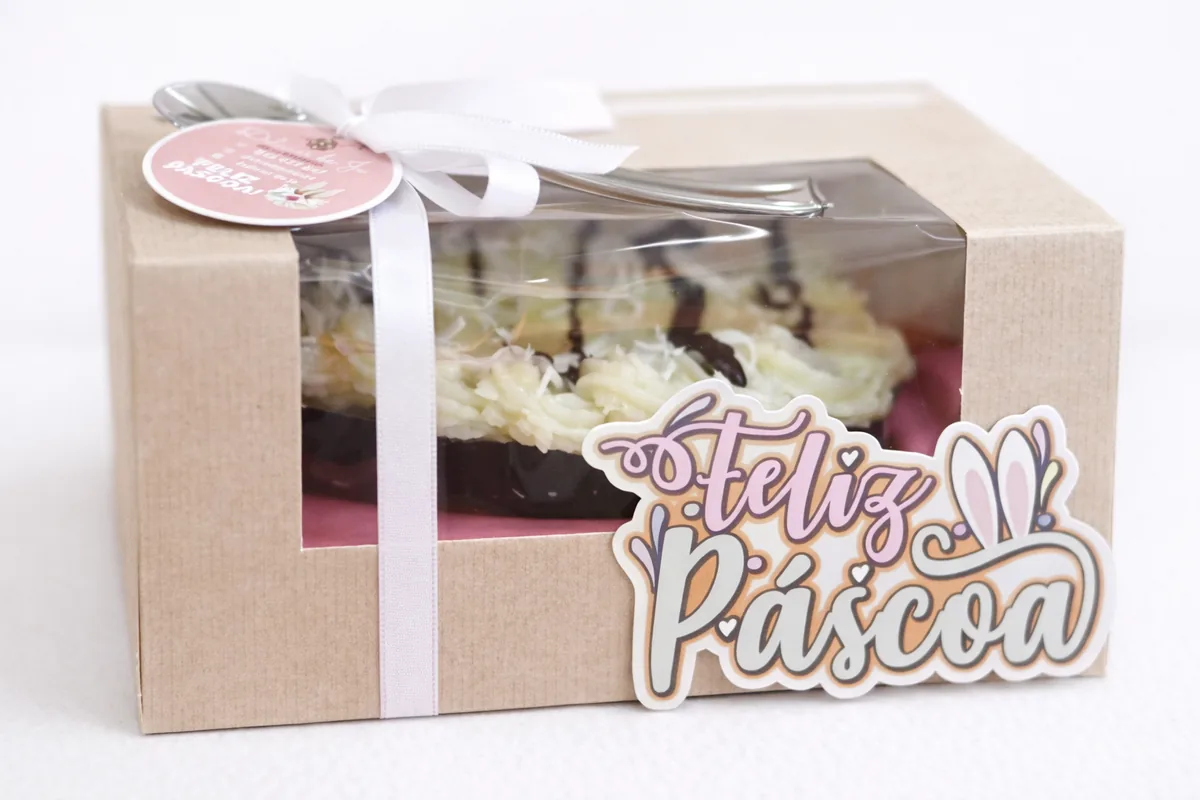 Caixa de bolo em cartão kraft com laço branco e placa Feliz Páscoa recortada em papel com orelhas de coelho