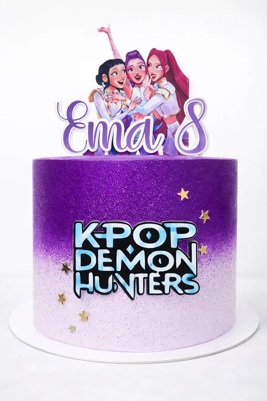 Bolo de aniversário roxo com topo em papel personalizado: o nome Ema, o número 8 e figuras recortadas